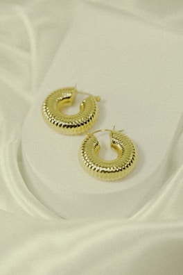A pair of shimmering hoop earrings placed on a marble surface.