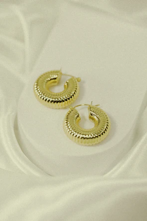 A pair of elegant gold hoop earrings displayed against a soft fabric background.