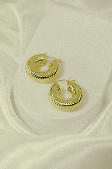 A close-up of delicate, lightweight gold hoop earrings resting on a soft linen cloth.
