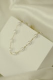 A delicate necklace with pearl-like beads and gold links is elegantly displayed on a minimalistic white surface. The soft lighting and subtle shadows add to the understated elegance.
