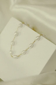 A stylish necklace with a subtle shine displayed draped over a minimalist white stand.