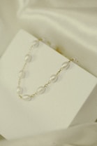 A delicate necklace with pearl-like beads and gold links is elegantly displayed on a minimalistic white surface. The soft lighting and subtle shadows add to the understated elegance.