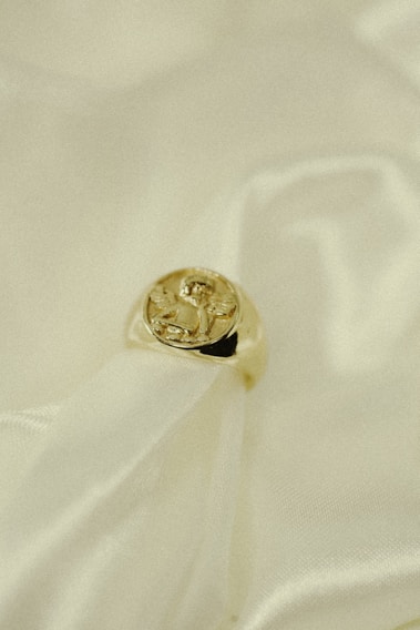 Close-up of a delicate silver ring with a subtle gold accent resting on soft beige fabric.