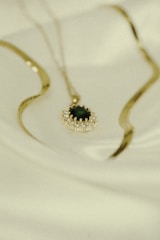 Close-up of a delicate gold necklace with a sparkling diamond pendant resting on a soft white fabric.