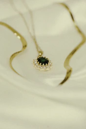 A delicate gold necklace with a sparkling pendant displayed on a velvet black cushion.