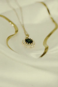 A close-up shot of a delicate gold necklace with a deep burgundy gemstone pendant resting on cream fabric.