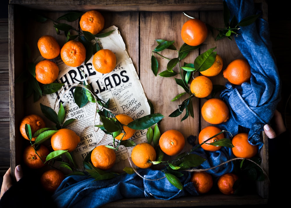 a wooden box filled with oranges next to a blue cloth
