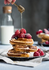 Close-up of a vibrant protein waffle topped with fresh berries and a drizzle of honey.