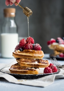 Protein waffles stacked high with fresh berries and a drizzle of honey, inviting and warm.