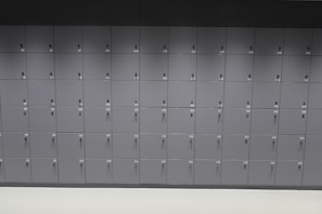 A wall consisting of multiple rows of grey lockers with sequential numbering on the doors. Each locker door has a keyhole, and the lockers are uniformly aligned.