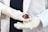 A person wearing white latex gloves holds a small red organic object, possibly a flower or plant part, with intricate details. The person is dressed in a white lab coat, suggesting a scientific or medical context.