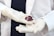 A person wearing white latex gloves holds a small red organic object, possibly a flower or plant part, with intricate details. The person is dressed in a white lab coat, suggesting a scientific or medical context.