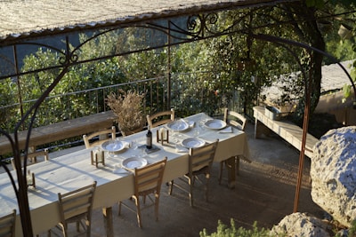 Rustic table set outdoors with local dishes and wine glasses under a pergola.