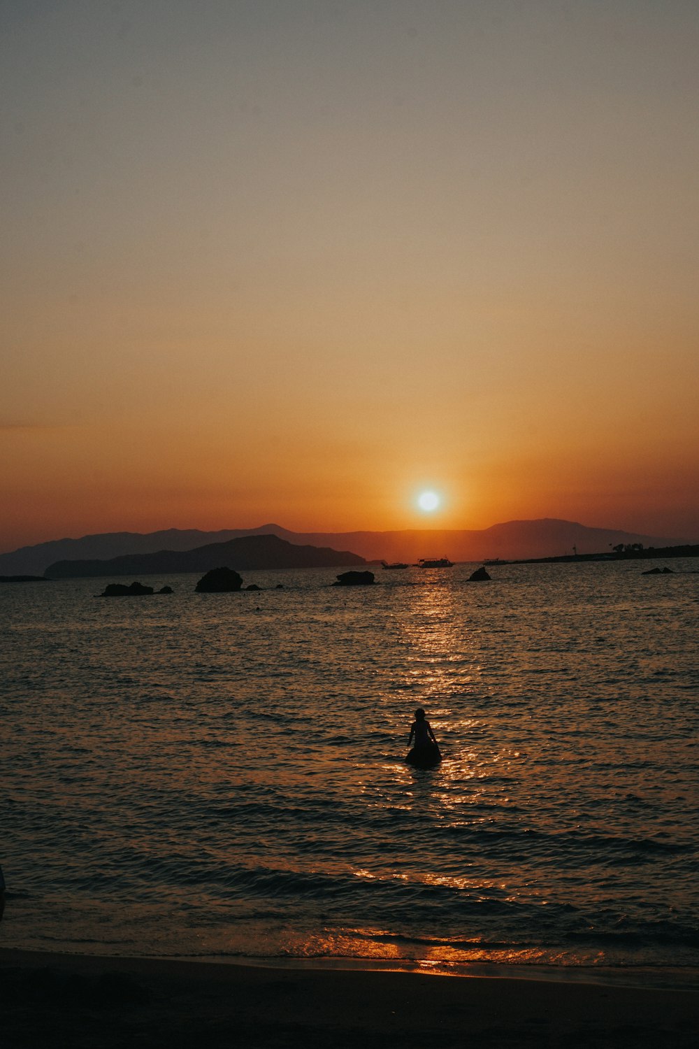 a person swimming in the ocean at sunset