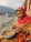 A smiling middle-aged woman in traditional Indian attire, standing near the Ganges riverbank at sunrise.