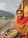 A smiling middle-aged woman sitting peacefully by the Ganga river at sunrise.
