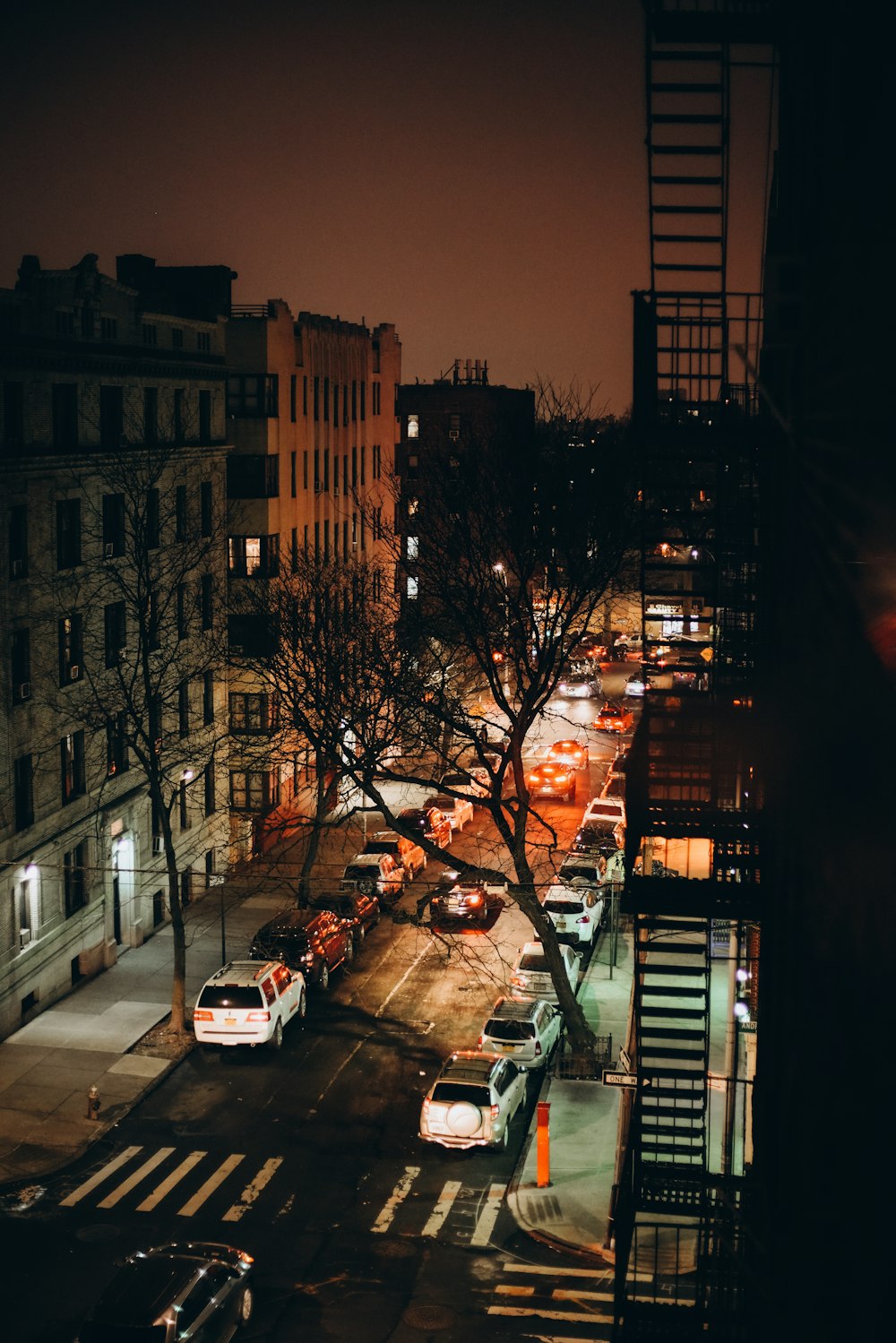 a city street at night with cars parked on the side of the road