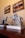 Several silver trophies featuring horse and rider sculptures are placed on a wooden surface, alongside a stack of magazines. Two framed pictures depicting scenes of horse riding are hung on the wall above.