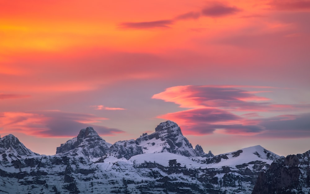 a mountain range covered in snow under a pink sky