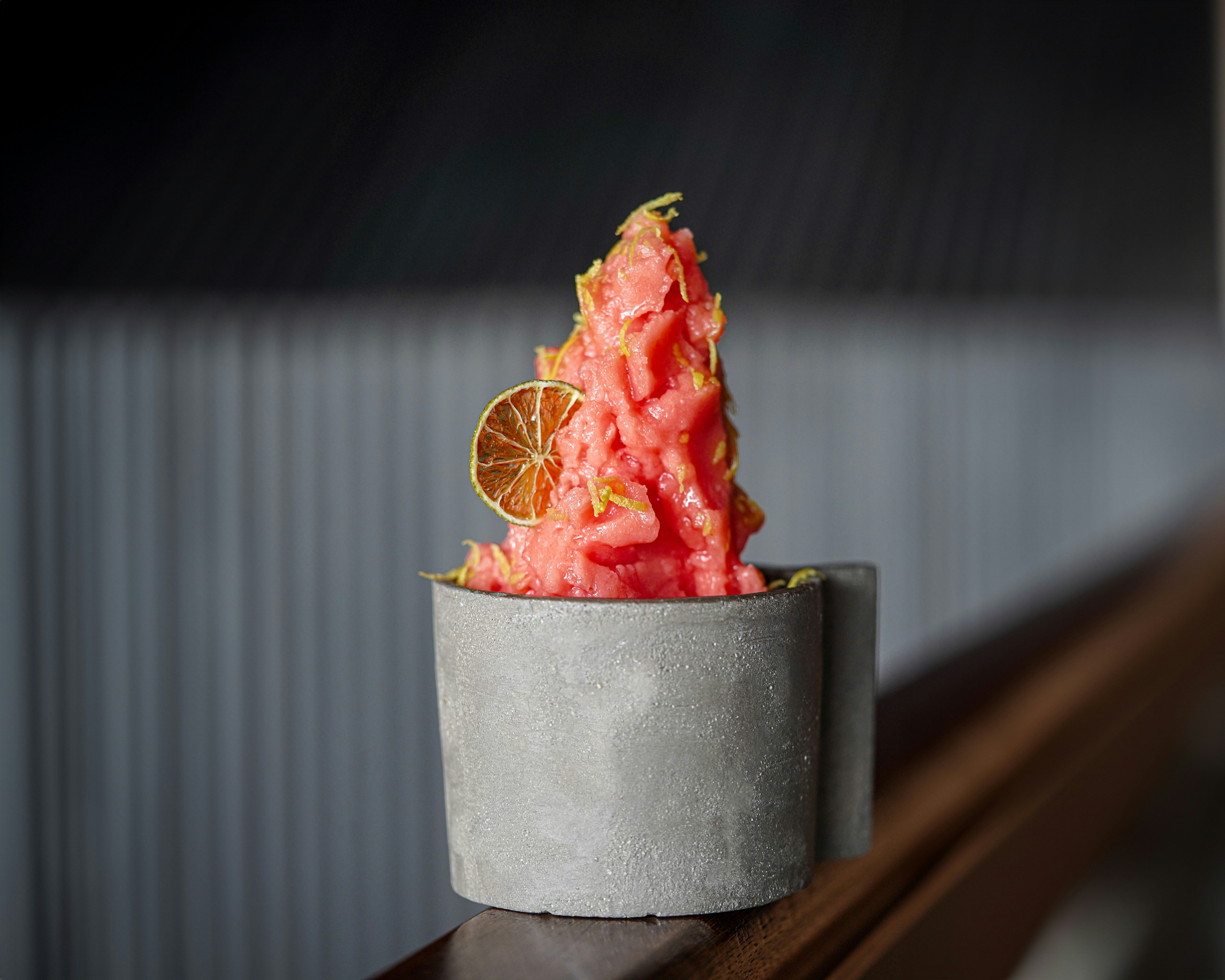 Soft pink guava lime sorbet in a pint container with fresh guava and lime slices beside it