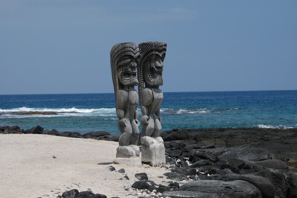 a couple of statues sitting on top of a sandy beach