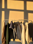 A collection of colorful casual shirts and sweaters hanging on a rack in natural light.