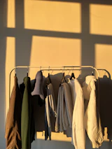 Brightly colored clothing pieces hanging on a rustic rack against a warm, sunlit wall.