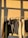 A row of various colored clothes hanging on a rack, with sunlight casting shadows on the wall behind. The garments include jackets, sweaters, and hoodies in neutral and earthy tones.