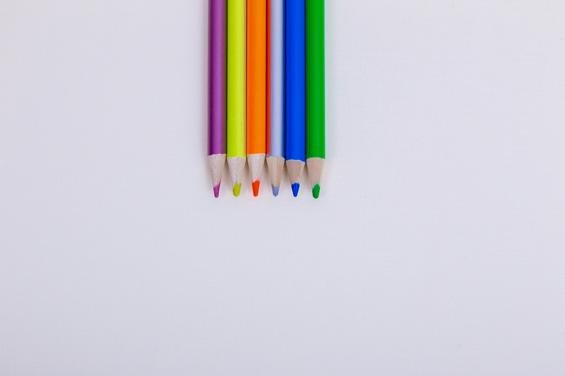 a row of colored pencils sitting on top of a white surface