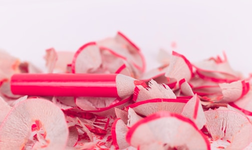 A close-up of a red pencil resting on a clean, white desk with sketches and notes scattered around.