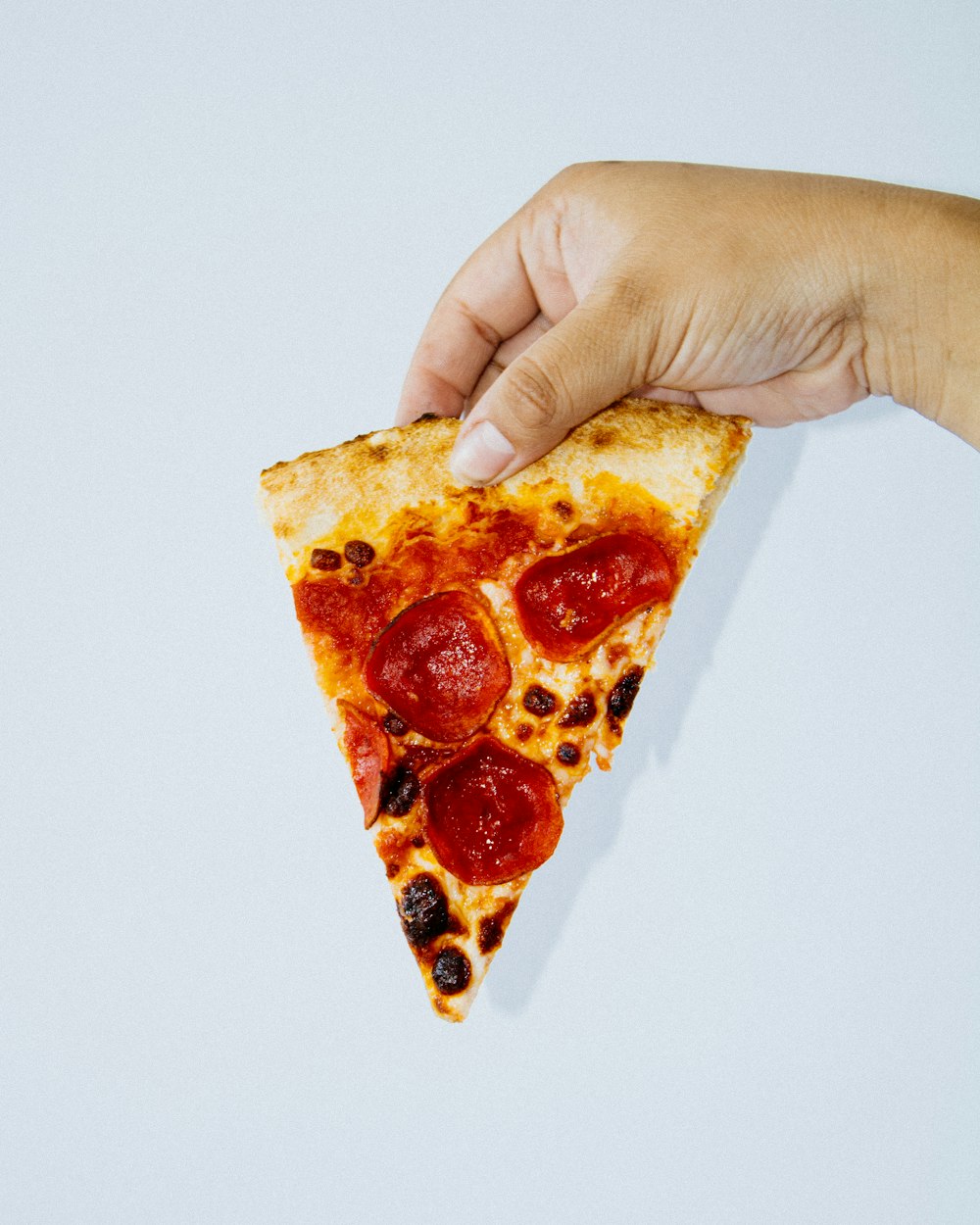 a hand holding a slice of pizza with pepperoni on it