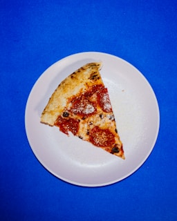 A vibrant, steaming pizza slice with bubbling cheese and bright orange accents on a dark plate.
