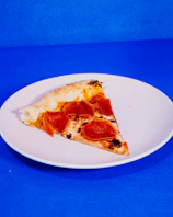 Hot pizza slice with bubbling cheese and pepperoni resting on a bright red plate.