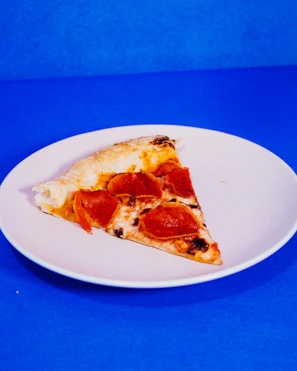 Hot pizza slice with bubbling cheese and pepperoni resting on a bright red plate.