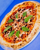 A freshly baked pizza with a bubbly crust, topped with melted cheese, tomato sauce, and garnished with vibrant green basil leaves. The pizza is placed on a blue surface.