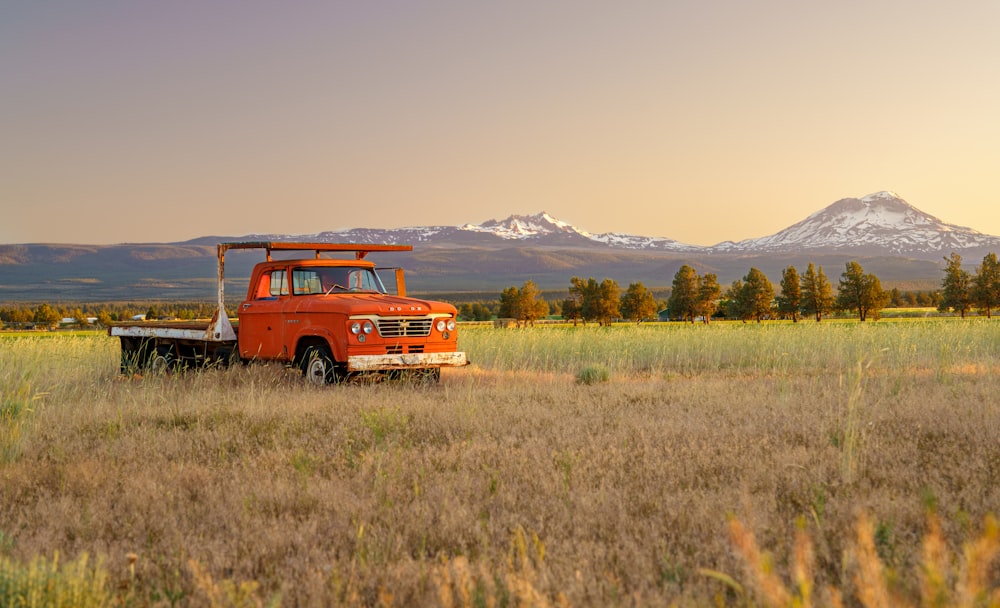 an orange truck parked in a field with mountains in the background
