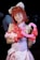 A person is dressed in a colorful, anime-inspired costume with cat ears and red hair, wearing a pink outfit with a detailed bow and holding a plush heart accessory.