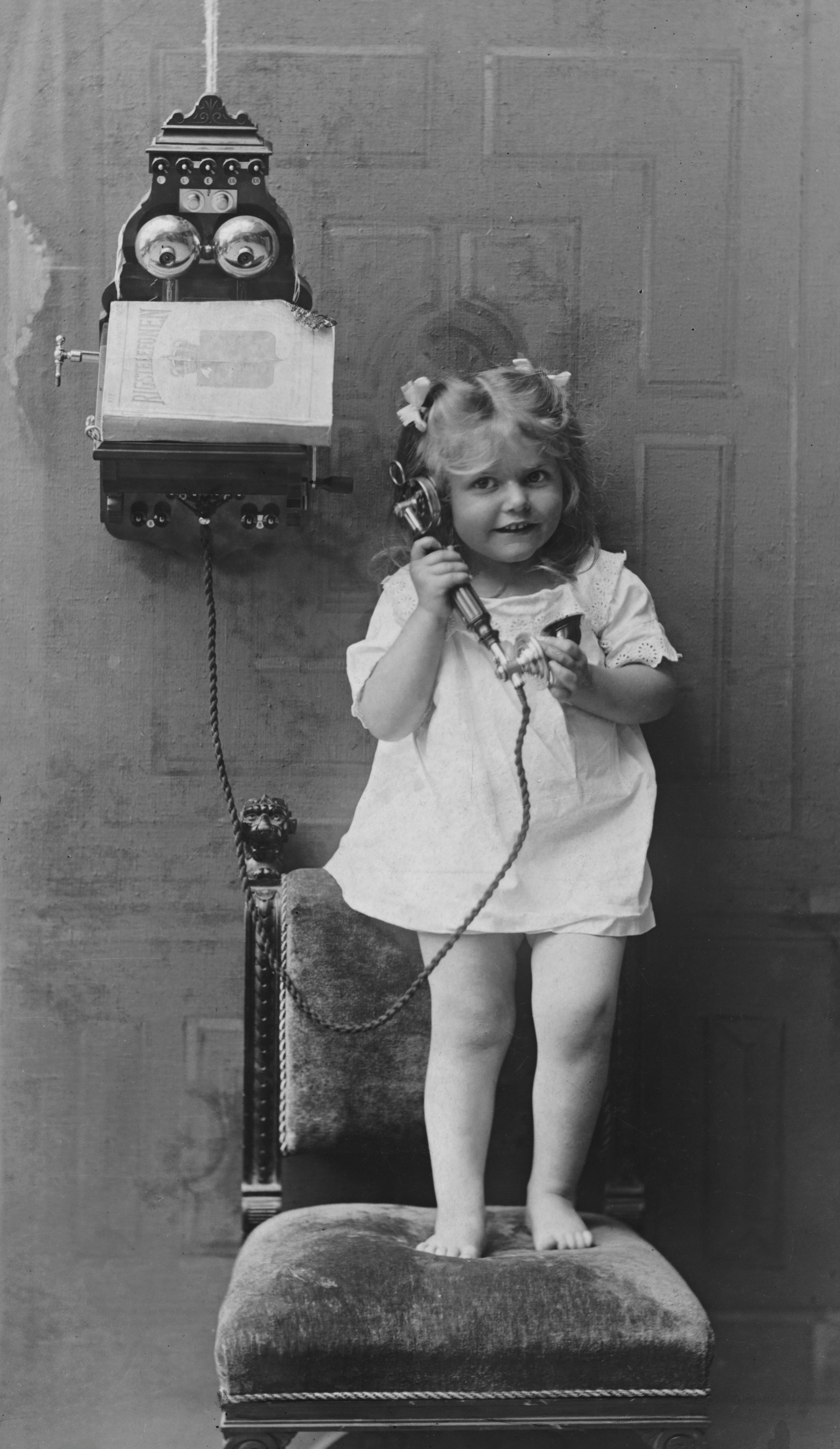 a little girl standing on a chair while talking on a phone