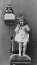 a little girl standing on a chair while talking on a phone