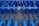 Industrial farming equipment with multiple rows of blue metal discs and blades arranged in a symmetrical pattern, against a gravel surface.
