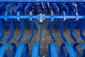 Industrial farming equipment with multiple rows of blue metal discs and blades arranged in a symmetrical pattern, against a gravel surface.