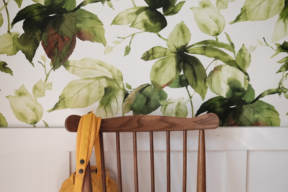 a wooden chair sitting in front of a wall with green leaves on it