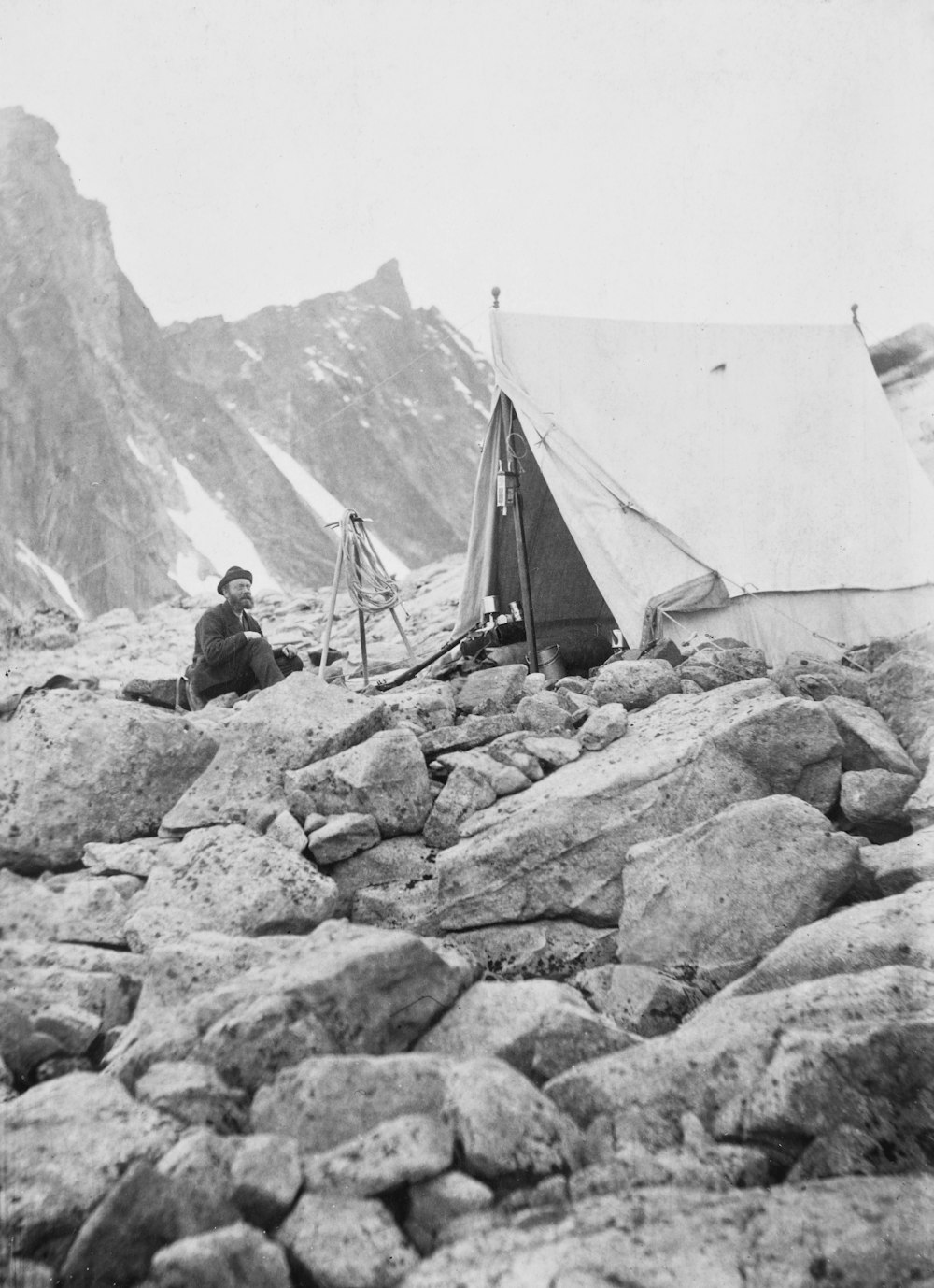 a man sitting next to a tent on top of a mountain