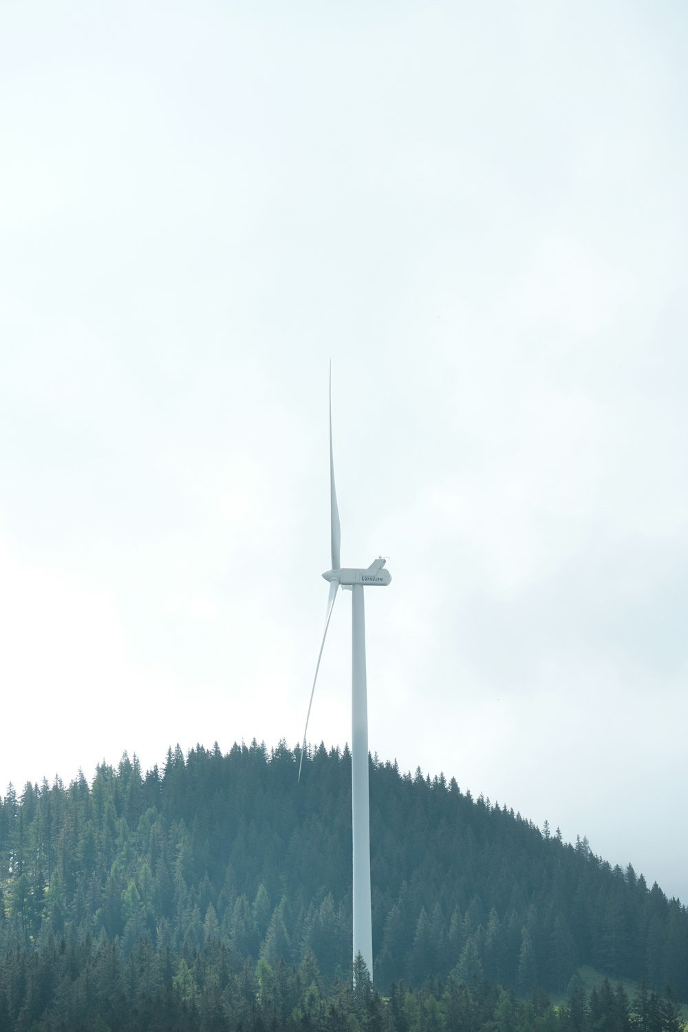 uma turbina eólica em uma colina com árvores ao fundo