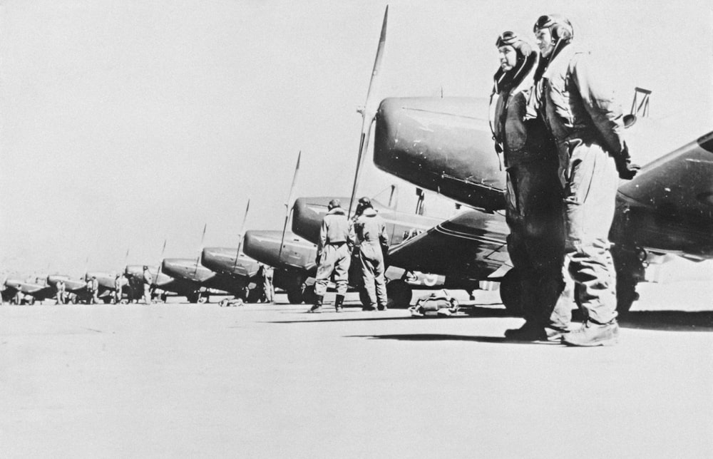 a black and white photo of men standing in front of airplanes