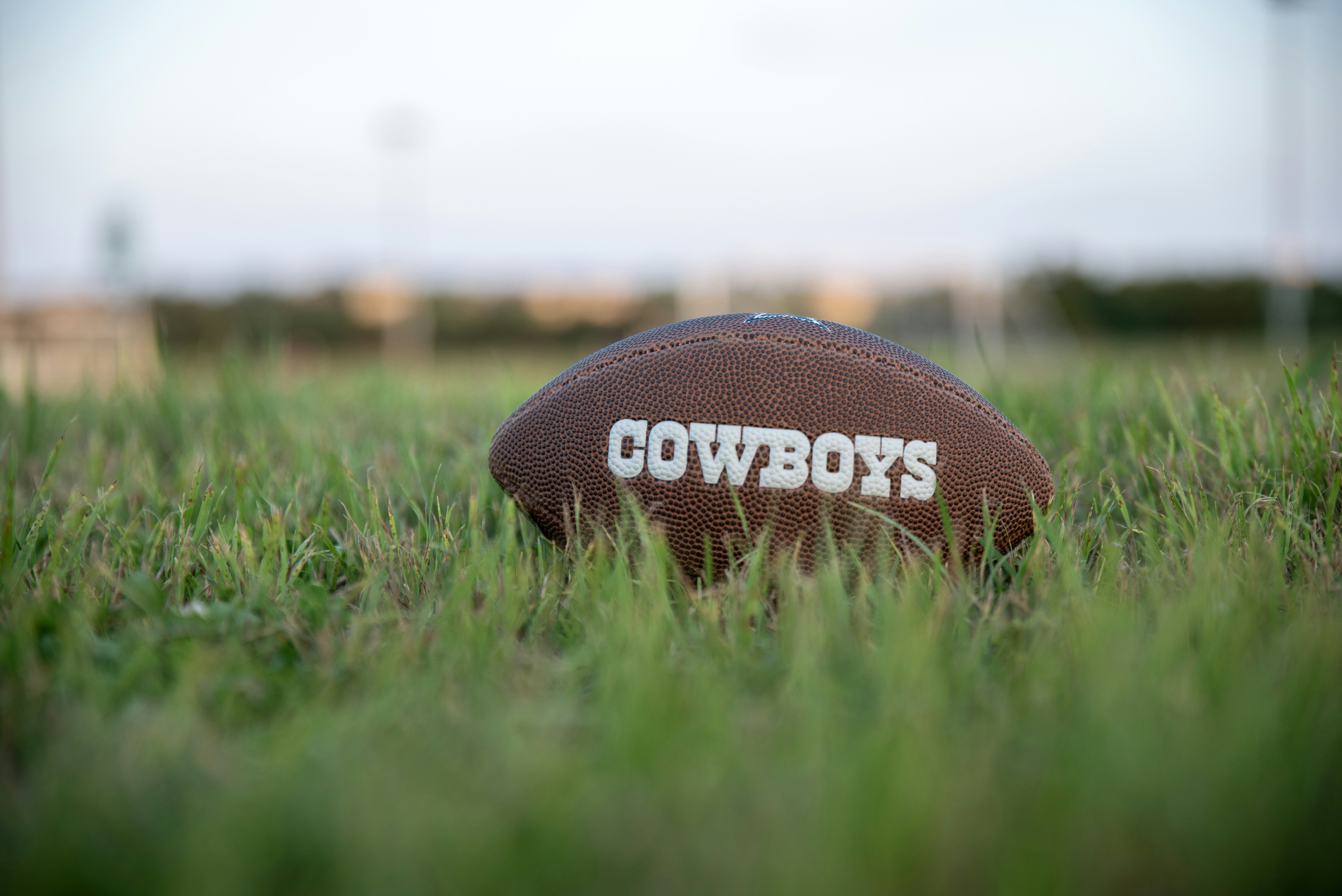 a football sitting in the grass with the word cowboys written on it