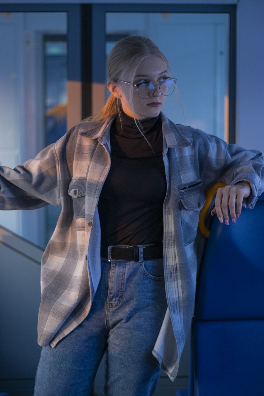 a woman wearing glasses leaning against a blue wall