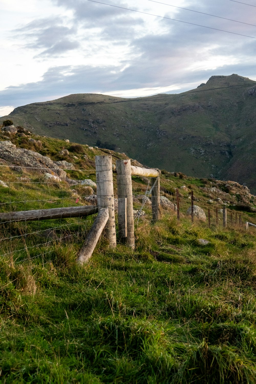 a wooden fence on a grassy hill with mountains in the background
