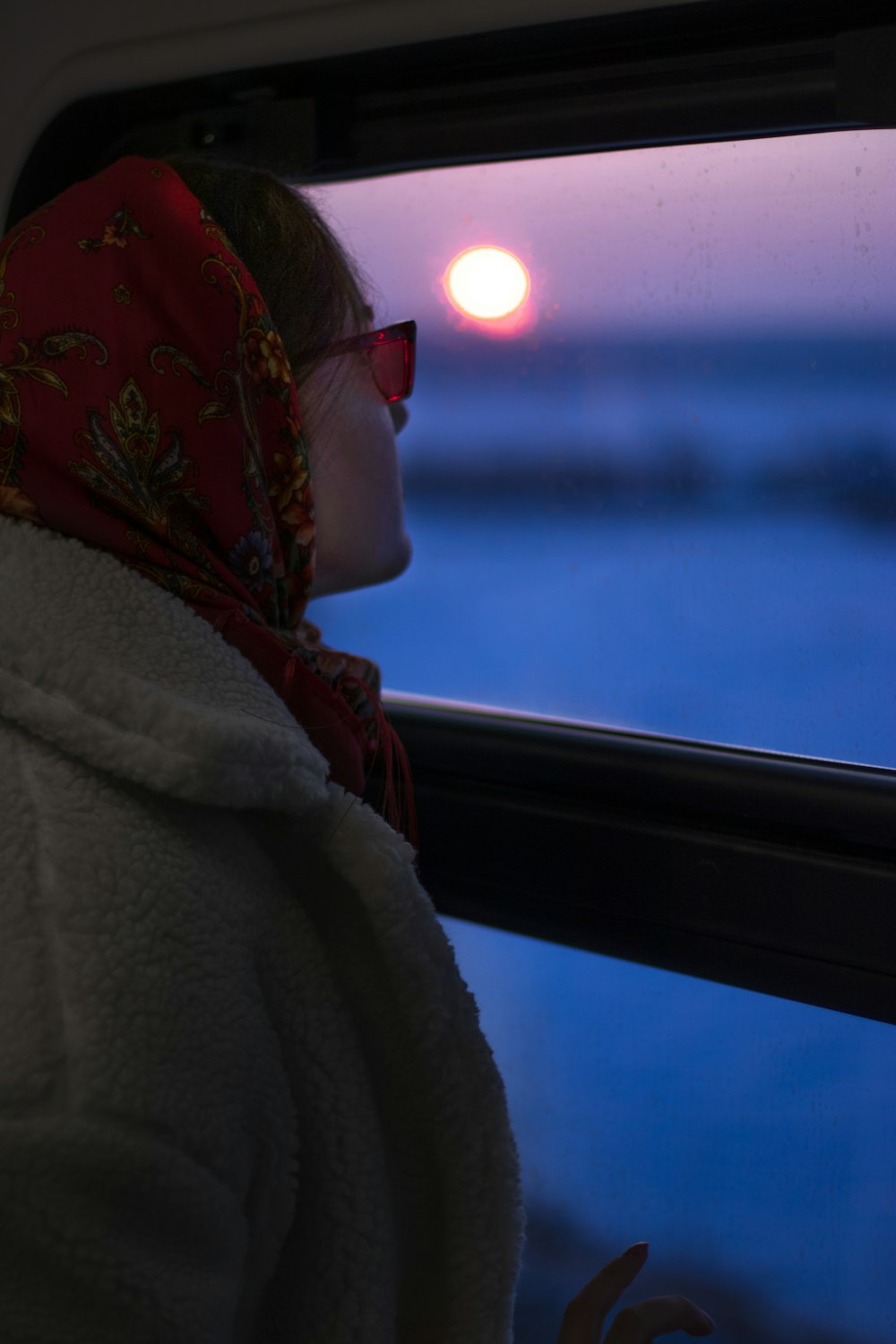 a woman looking out a window at the sunset