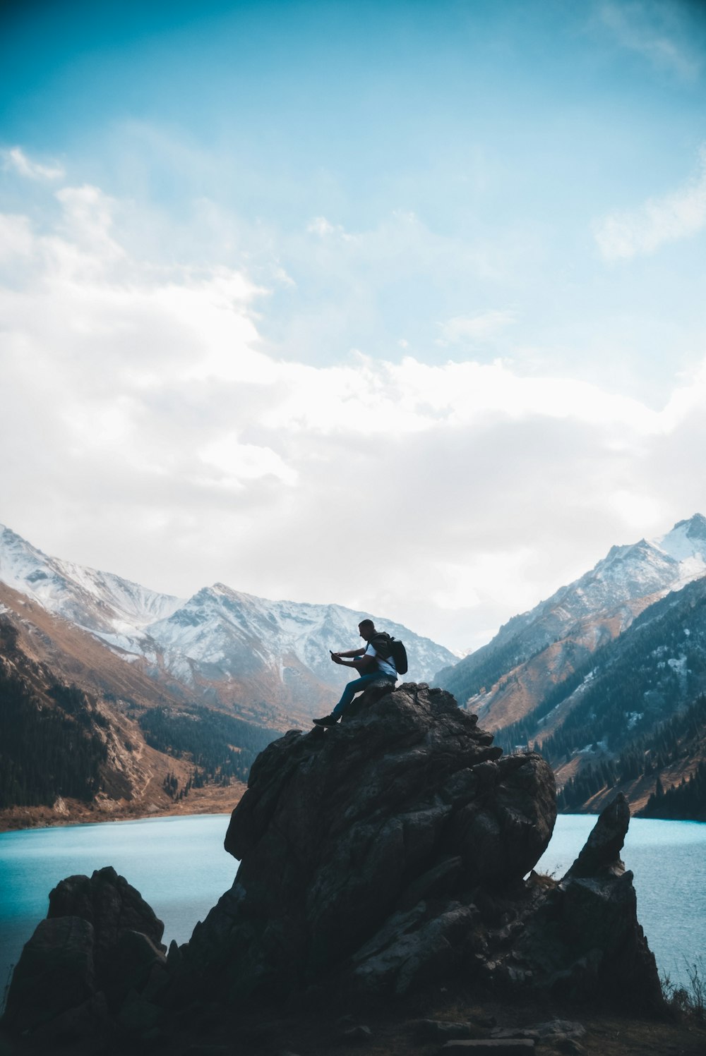 a person sitting on top of a rock next to a lake